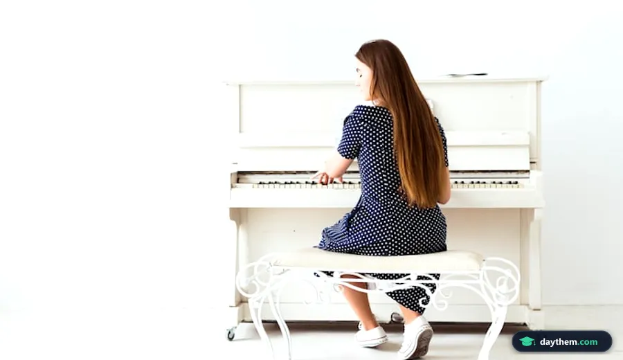 Cô gái trẻ tóc dài ngồi quay lưng bên đàn piano cơ đặt cạnh bức tường trắng