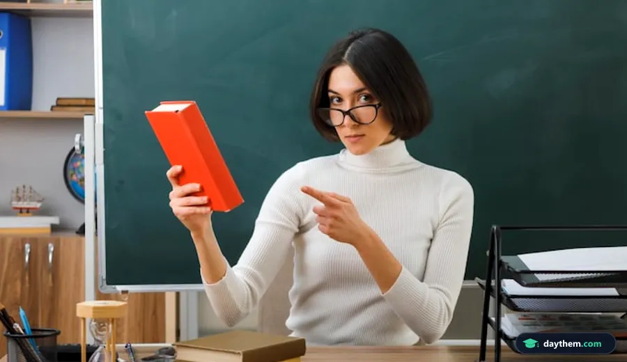 Nữ giáo viên đeo kính ngồi bên bàn làm việc, tay chỉ vào cuốn sách mở để chuẩn bị hồ sơ chuyên môn và kế hoạch bài dạy